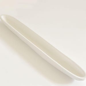 May include: A long, off-white ceramic serving dish with a gently curved shape. The dish is empty and has a smooth, glossy finish. The design is simple and modern, suitable for serving appetizers or snacks.