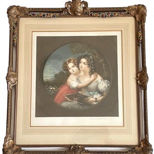 May include: Framed print featuring two women in a romantic embrace, set within an oval scene. The artwork is in a gold ornate frame with decorative accents. The women are dressed in period clothing, with a landscape background.