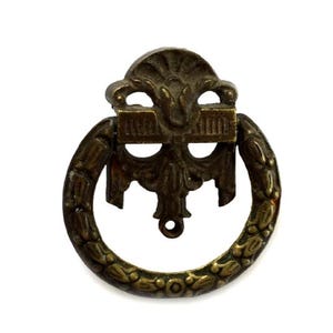 May include: Antique brass drawer pull with a decorative design. The pull features a circular handle with a laurel leaf pattern and an ornate backplate. The hardware is made of metal and has a vintage aesthetic.
