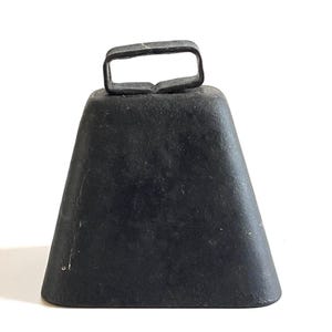 May include: A black, trapezoid-shaped bell with a rectangular handle. The bell has a slightly textured surface and a dark, matte finish. The handle is made of the same material as the bell. The bell is likely made of metal.