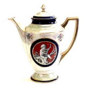 May include: Antique white porcelain teapot with a gold handle and accents. The teapot features a round medallion with a cherub playing a stringed instrument against a red background, framed by a blue border.