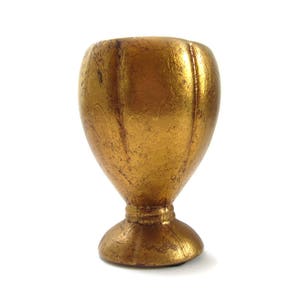 May include: A golden-colored, egg-shaped decorative cup with a pedestal base. The cup has a textured surface and is set against a white background. The cup is likely made of metal or a similar material.