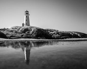 May include: A black and white photograph of a tall, cylindrical lighthouse standing on a large, smooth rock formation. The lighthouse features a lantern room at the top and is reflected in a calm pool of water in the foreground of the scene.
