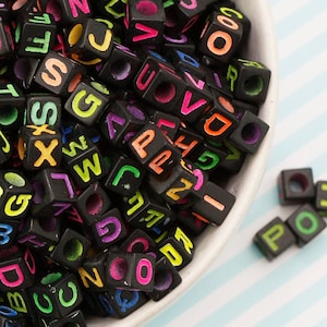 May include: A bowl filled with black letter beads with colourful letters. The beads are in a random order and are all the same size.