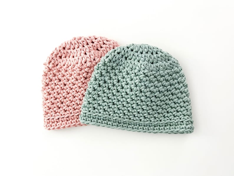 May include: Two crocheted hats, one in a light pink colour and the other in a light green colour.