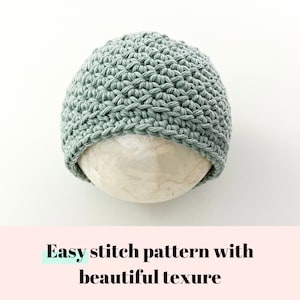 May include: A sage green crocheted beanie hat with a textured stitch pattern. The hat is displayed on a white surface.