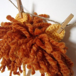 May include: A crocheted lion mane with orange and yellow yarn, hanging from a clothesline with wooden clothespins.