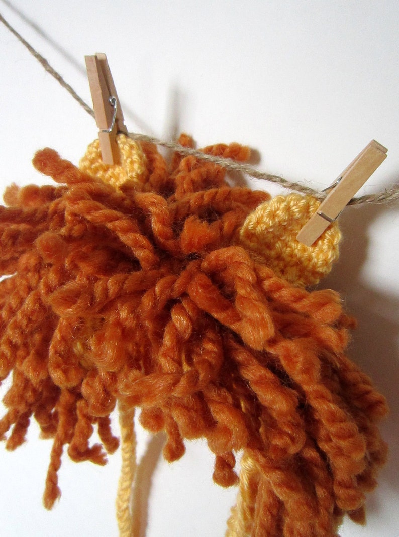 May include: A crocheted lion mane with orange and yellow yarn, hanging from a clothesline with wooden clothespins.