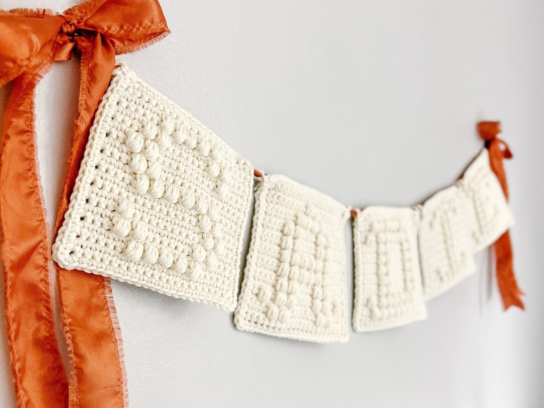 May include: A white crocheted banner with the word "LOVE" spelled out in individual squares. The banner is strung with orange ribbon.