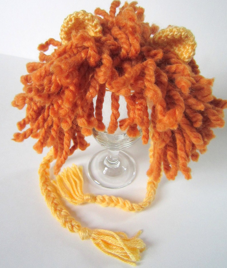 May include: A crocheted lion mane hat with orange and yellow yarn. The hat has two long yellow tails.