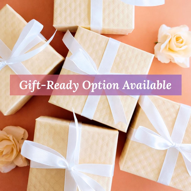 Puede incluir: Varias cajas de regalo con un patr&oacute;n acolchado est&aacute;n dispuestas sobre una superficie naranja. Cada caja est&aacute; atada con una cinta de raso blanca. El texto "Gift-Ready Option Available" se muestra en una pancarta p&uacute;rpura.