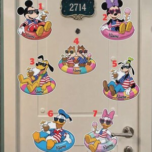 May include: A set of seven decorative wall decals featuring cartoon characters in swim rings, numbered one through seven. Each character wears sunglasses and a red, white, and blue shirt, holding a drink or ice cream. Each decal includes a name label.