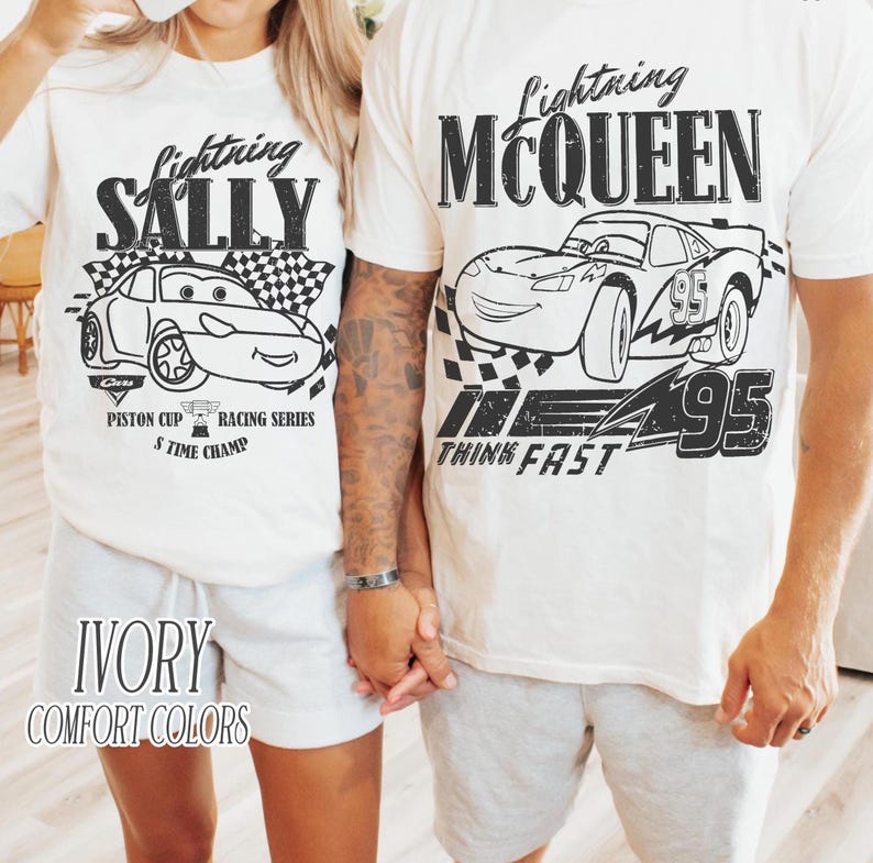May include: Two ivory t-shirts featuring black graphic prints. The left shirt displays Lightning Sally with the text Lightning SALLY PISTON CUP RACING SERIES 5 TIME CHAMP. The right shirt shows Lightning McQueen with the text Lightning MCQUEEN THINK FAST 95.