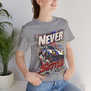 May include: A heather gray short-sleeve t-shirt featuring a graphic print of a white, blue, and red sports car with the number 77. The design includes the text NEVER SETTLE, BUILT TO MOVE, and LIMITS ARE OPTIONAL, along with Japanese characters.