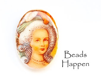 May include: Oval-shaped glass bead featuring a painted image of a woman wearing a white wig and a hat with floral accents. The bead has a yellow-orange tint.