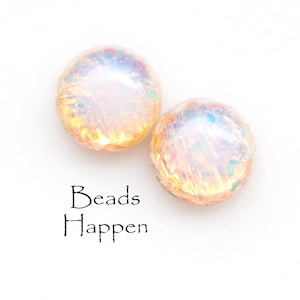 May include: Two iridescent round beads with a gold shimmer. The beads are on a white background. The text "Beads Happen" is written below the beads.