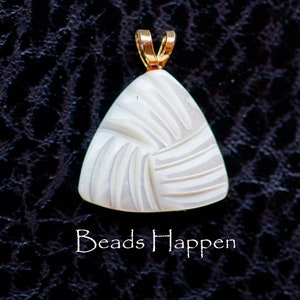May include: White carved pendant with a gold bail. The pendant is shaped like a triangle and has a swirling pattern. The pendant is on a black background.