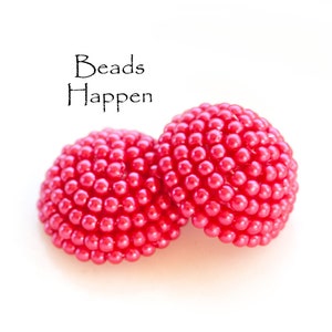 Op de afbeelding: Twee felrode, koepelvormige objecten bedekt met kleine, ronde kralen. De objecten staan tegen een witte achtergrond. De tekst "Beads Happen" staat in zwart script boven de objecten.