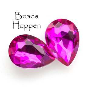 Puede incluir: Dos cuentas de vidrio de color rosa en forma de l&aacute;grima con un dise&ntilde;o facetado. Las cuentas est&aacute;n sobre un fondo blanco. El texto "Beads Happen" est&aacute; escrito encima de las cuentas.