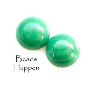 May include: Two green glass cabochon beads. The beads are round and have a smooth, glossy finish. The text "Beads Happen" is printed below the beads.