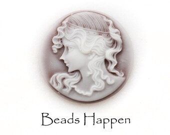 May include: A white cameo featuring a woman's profile with detailed hair and a brown background. The cameo is oval shaped and has a smooth, polished surface. The text "Beads Happen" is printed below the cameo.