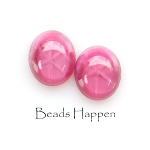Puede incluir: Dos cuentas de vidrio ovaladas de color rosa con un diseño de estrella en relieve. Las cuentas son brillantes y tienen un ligero brillo iridiscente.