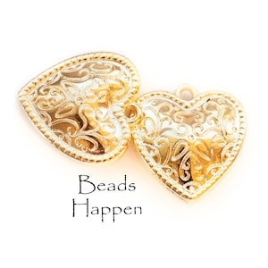 Könnte beinhalten: Zwei goldene herzförmige Anhänger mit filigranen Blumenmustern. Die Anhänger sind perfekt für die Schmuckherstellung oder um handwerklichen Arbeiten einen Hauch von Eleganz zu verleihen.