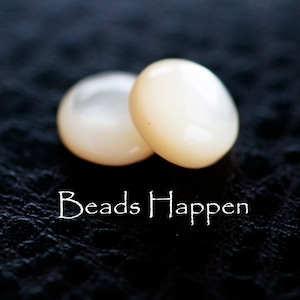 May include: Two white round beads with a smooth, pearlescent finish. The beads are on a black surface with the text "Beads Happen" written in white.