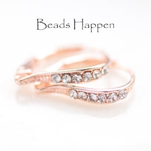 May include: A pair of rose gold hoop earrings with a row of clear rhinestones on each hoop. The earrings are on a white surface. "Beads Happen" is written in black text above the earrings.