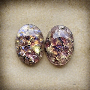 May include: Two oval-shaped iridescent glass cabochons with a crackled, textured surface. The cabochons have a mix of purple, pink, and gold colors.