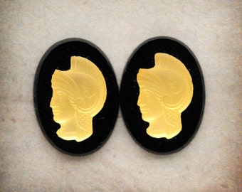 May include: Two black oval-shaped cameo earrings with gold-coloured profile images of a person wearing a helmet.
