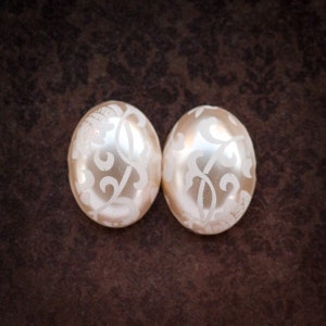 May include: Two white pearl-like earrings with a delicate floral design.