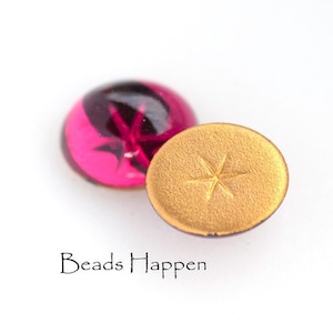 Może przedstawiać: Dwa okrągłe szklane kaboszony, jeden jest różowy z czarnym wzorem gwiazdy, a drugi jest złoty z wzorem gwiazdy.