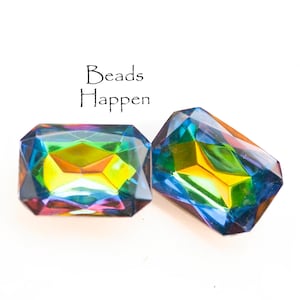 May include: Two iridescent faceted glass beads in a rectangular shape with a rainbow of colors, including blue, green, yellow, and orange. The text "Beads Happen" is written above the beads.