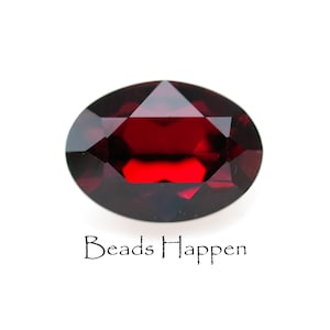 May include: A faceted, oval-shaped, deep red gemstone. The gem is polished and set against a white background. The text "Beads Happen" is written in a cursive font below the gemstone.