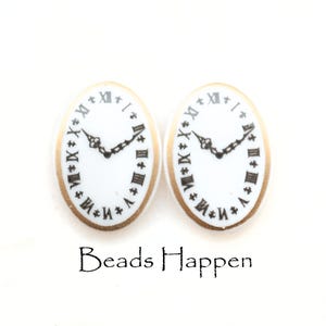 May include: A pair of white oval-shaped earrings with a gold rim and a black clock face with Roman numerals.