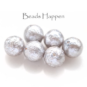 Puede incluir: Seis cuentas redondas de color plateado con una superficie texturizada. Las cuentas tienen un agujero en el centro para enhebrar.