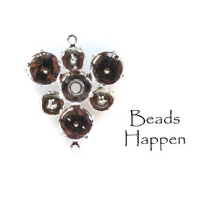 Puede incluir: Un grupo de tapas de cuentas de metal plateadas con un bucle en la parte superior. El texto "Beads Happen" está impreso debajo de las tapas de cuentas.