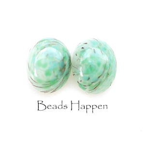 May include: Two round, green glass beads with white and brown swirls. The beads have a speckled appearance.