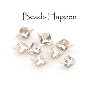 May include: Eight clear, faceted, square-shaped beads on a white background. The text "Beads Happen" is written above the beads.