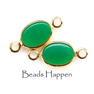 May include: Two oval-shaped green gemstone beads with gold-toned metal loops on each side. The beads are connected to each other by the loops. The text "Beads Happen" is visible below the beads.