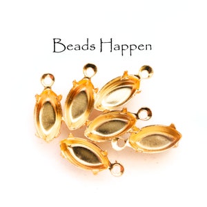 May include: Six gold-toned metal bead caps with a loop at the top. The caps are oval shaped with a pointed edge.