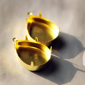 May include: Two gold-colored metal earring settings with a rounded oval shape. The settings have a smooth, shiny finish and are designed to hold a cabochon stone.