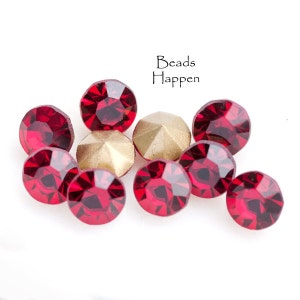 May include: A group of ten red crystal rhinestones, some with gold settings, on a white background. The text "Beads Happen" is visible above the rhinestones.