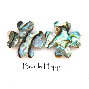 May include: Two iridescent abalone shell flower-shaped charms with a green, blue, and brown color pattern. The charms are on a white background. Beads Happen is written below the charms.