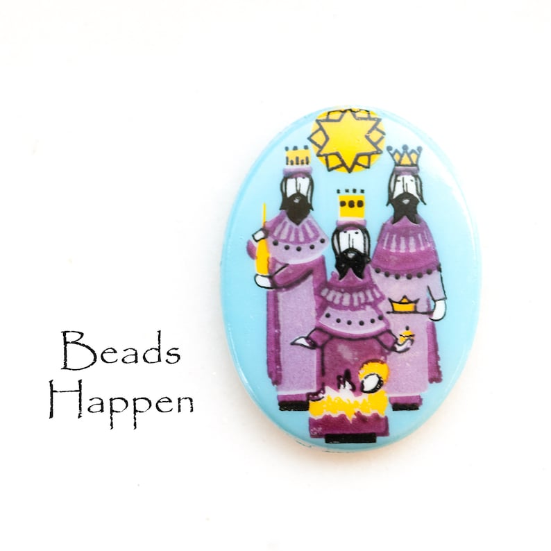 May include: A blue oval-shaped Christmas ornament with a depiction of the three wise men in purple robes, carrying gifts and following a yellow star.