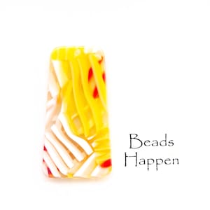 Puede incluir: Una cuenta de vidrio amarilla, blanca y roja con un patrón de rayas. La cuenta es de forma rectangular y tiene un agujero en la parte superior para enhebrar. El texto "Beads Happen" está escrito debajo de la cuenta.
