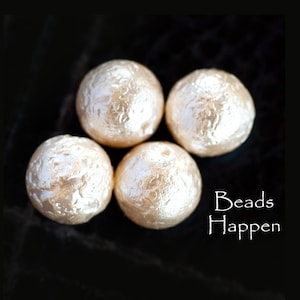 Puede incluir: Cuatro cuentas redondas de color blanco roto con una superficie texturizada. Las cuentas están dispuestas en forma de triángulo sobre un fondo negro. El texto "Beads Happen" está escrito en blanco debajo de las cuentas.