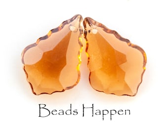 May include: Two amber-colored crystal teardrop-shaped beads with a faceted design. The beads have a slightly wavy edge. Beads Happen is written in black text below the beads.