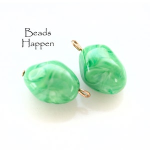May include: Two green swirl glass beads with gold jump rings. Beads Happen.